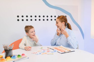 Kart ve eğitim araçları kullanan bir bayan öğretmenle yapılan konuşma terapisi sırasında telaffuz üzerine çalışan genç bir çocuk