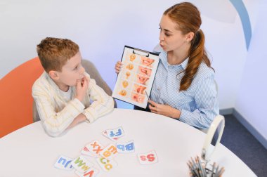 Kadın konuşma terapisti, bir dil terapisi sırasında görsel araçlar kullanarak erkek çocuğa konuşma ve konuşma geliştirme öğretiyor.