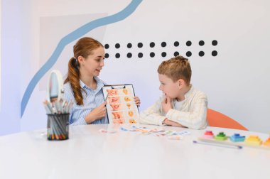 Gelişim terapisi seansında genç bir çocuğa ağız egzersizleri ve duygusal kartlar gösteren terapist.