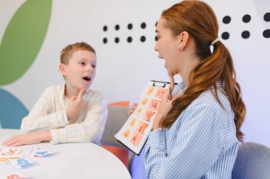 Konuşma patologu, bir terapi seansında görsel araçlar kullanarak telaffuz ve iletişim becerilerini geliştirmek için genç bir çocukla birlikte çalışıyor.