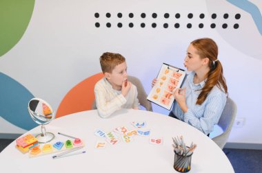 Konuşma terapisti küçük bir çocuğa konuşma geliştirmede yardım ediyor, görsel araçlar kullanıyor ve öğrenme seansı sırasında eklem egzersizleri yapıyor.