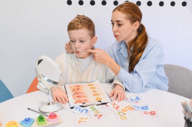Konuşma terapisti çocuğun konuşma gelişimine yardım ediyor. Küçük çocuk terapi sırasında aynaya bakarak düzgün ağız hareketleri öğreniyor.