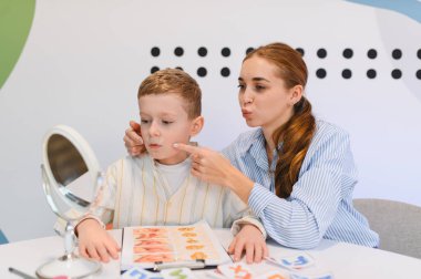 Çocuk seans sırasında görsel ipuçları ve ayna kullanarak terapistle konuşma dili ve iletişim becerileri öğreniyor.