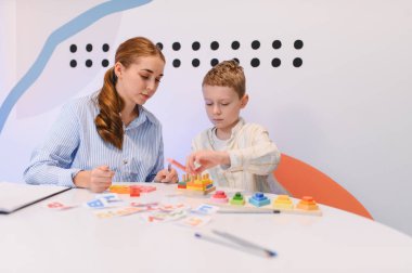 Erken eğitim sırasında erkek çocuğa ahşap sıralama taşları ve alfabetik harflerle öğretmenlik yapan kadın.