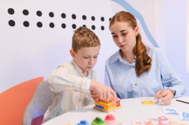 Eğitim engelleriyle oynayan genç bir çocuk, terapi seansı sırasında gelişimine rehberlik eden şefkatli bir öğretmen.