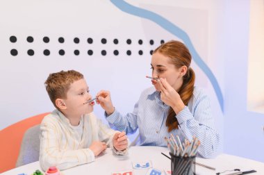 Konuşma terapisti, kalem kullanarak, konuşma geliştirme ve öğrenme üzerine yoğunlaşarak konuşma egzersizleri yapan genç bir çocuğa yardım ediyor.