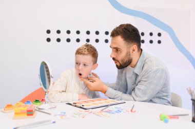 Konuşma terapisti, terapi seansında küçük bir çocuğa konuşma egzersizleri, konuşma becerileri ve iletişim becerileri konusunda yardım ediyor.