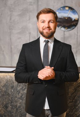 Elleri sımsıkı bağlı, sakallı bir yönetici gülümseyerek profesyonelliği, başarıyı ve kurumsal bir ortama güveni resmediyor.