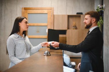 Konuk, resepsiyondaki gülümseyen bir otel çalışanından konukseverliği ve hizmeti simgeleyen bir anahtar kartı alıyor.