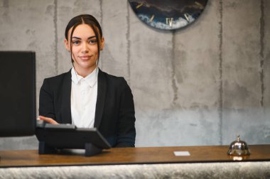 Tezgahta duran dost canlısı resepsiyonist modern bir otel lobisinde profesyonel konukseverlik hizmeti sunuyor.