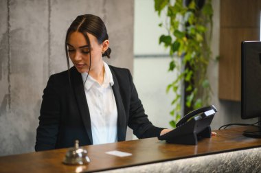 Modern bir otel lobisinde resepsiyonist olarak çalışan genç profesyonel resepsiyonist, kapıcı ve müşteri hizmetleri sunar.