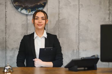 Otel kapıcısı olarak çalışan genç bir kadın resepsiyonda beklerken profesyonel konukseverlik hizmeti veriyor.