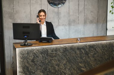 Modern bir otel lobisinde dost canlısı bir resepsiyonist, müşterilere soruşturmalarında yardımcı oluyor.