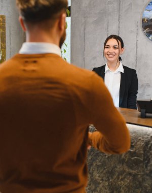 Gülümseyen kadın resepsiyonist, modern otel resepsiyonunda bir konuğa yardım ediyor. Müşteri hizmeti ve konukseverlik sağlama