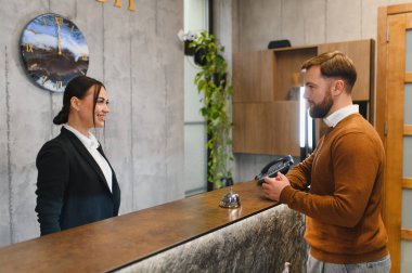 Dost canlısı otel resepsiyonisti, resepsiyonda bir erkeğe yardım ediyor. Giriş sırasında konukseverlik hizmeti veriyor.