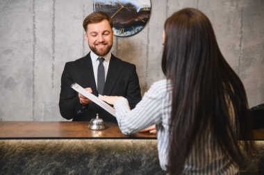 Dostane otel resepsiyonisti, modern resepsiyon masasına kayıt yaptıran bir müşteriye dostane bir belge veriyor.