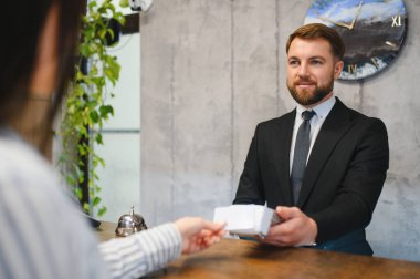 Dost canlısı otel resepsiyonisti resepsiyondaki bir konuğa anahtar kartlarını veriyor ve mükemmel bir konukseverlik hizmeti sunuyor.