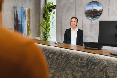 Modern otel lobisinde müşteri hizmetlerinde çalışan cana yakın genç bir bayan. Misafirperver profesyonel yardımcı ziyaretçi