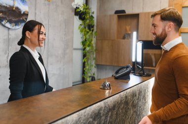 Otel resepsiyonisti, resepsiyonda bir erkeğe servis yaparken gülümseyerek mükemmel müşteri hizmetleri ve konukseverliğin altını çiziyor.