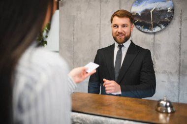 Resepsiyondaki bir konuğa oda anahtarı verirken gülümseyen otel kapıcısı konukseverlik hizmeti veriyor.