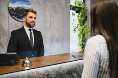 Otel girişinde, erkek resepsiyonist, kadın yolcuyu selamlıyor. Harika müşteri hizmetleri sunuyor.