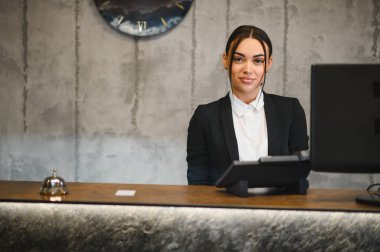 Resepsiyonda çalışan arkadaş canlısı bir kadın. Çağdaş otel lobisinde profesyonel müşteri hizmetleri sunuyor.