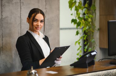 Genç iş kadını, modern bir otel resepsiyonunda profesyonel konukseverlik hizmeti sunuyor.
