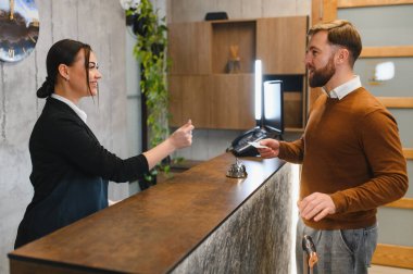 Resepsiyonist, modern bir otele giriş yapan erkek bir müşteriye anahtar kartı veriyor.