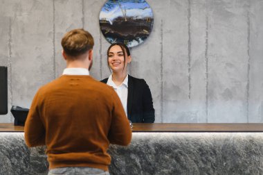 Dost canlısı otel resepsiyonisti gülümsüyor, modern resepsiyonda bir erkeğe yardım ediyor, mükemmel bir konukseverlik hizmeti sunuyor.