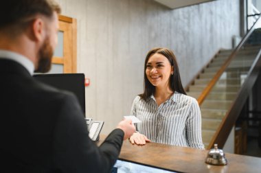 Otel resepsiyonisti gülümsüyor, resepsiyondaki mutlu bir bayana anahtar kartı veriyor, mükemmel bir konukseverlik hizmeti sunuyor.