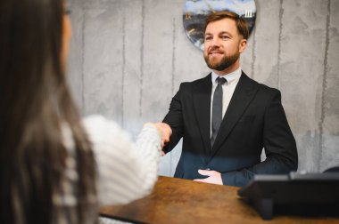 Otel müdürü ya da resepsiyonist resepsiyonda bir kadınla el sıkışıyor ve profesyonel konukseverlik hizmeti veriyor.