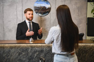 Erkek otel resepsiyonisti resepsiyonda bir bayanı karşılıyor ve ona konukseverlik ve hizmet sunuyor.