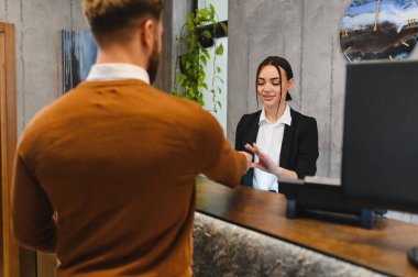 Adam modern bir lobide neşeli bir resepsiyonistle konuşuyor, profesyonel hizmet ve yardım alıyor.