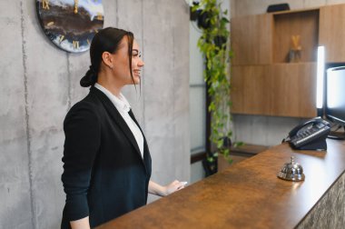 Gülümseyen kadın resepsiyonist, konukseverlik hizmeti sunuyor, modern bir otel veya ofis masasında müşterilere yardım ediyor.