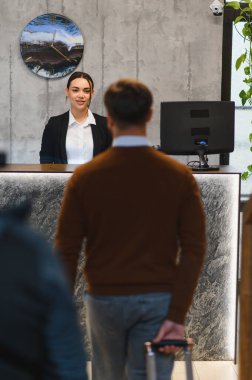Otel resepsiyonunda bekleyen dost canlısı resepsiyonist, kontrol sırasında tramvay bagajıyla gelen bir adamı karşılıyor.