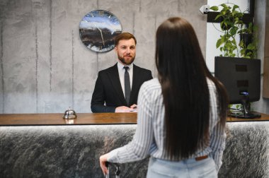 Otel resepsiyonunda duran müşteri, modern lobiye gelen müşterilere hizmet veren bir erkek resepsiyonist.