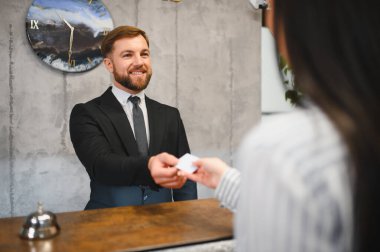 Resepsiyondaki arkadaş canlısı otel resepsiyonisti konaklama hizmeti için anahtar kartı veriyor.