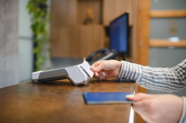 Bir oteldeki bir ödeme terminalinde kredi kartıyla güvenli bir mali işlem yapan bir kadın.