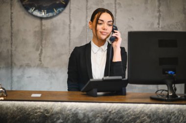 Modern resepsiyondaki sabit hattan müşteri hizmetleri sağlayan ve iletişimi yöneten profesyonel bir kadın.