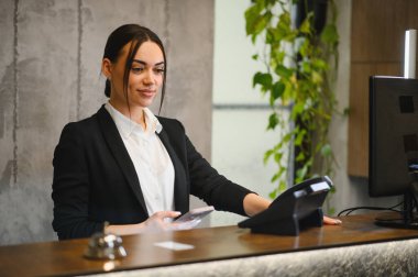 Resepsiyonda duran profesyonel bayan resepsiyonist konukseverlik ortamında mükemmel müşteri hizmetleri sunuyor.