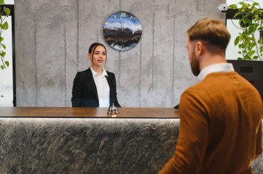 Kadın resepsiyonist, modern bir otel resepsiyonunda, profesyonel hizmet sunan bir erkeğe yardım ediyor.