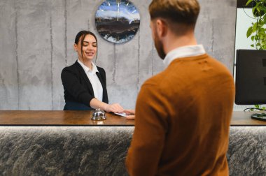 Dost canlısı otel resepsiyonisti, modern çekteki bir erkek konuğa anahtar kartı veriyor, mükemmel hizmet veriyor.