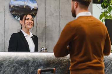 Otel resepsiyonunda müşteriyle konuşan arkadaş canlısı bir konukseverlik çalışanı modern bir lobide kaliteli hizmet sunuyor.