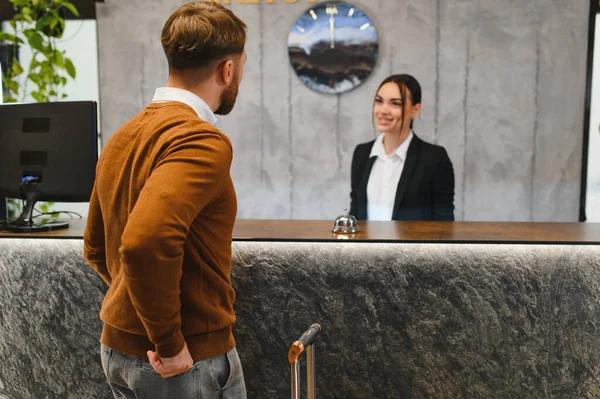 Bagajlı bir adam otele giriş yapıyor ve gülümseyen bir kadın resepsiyonistle konuşuyor. Çağdaş bir lobide konukseverlik hizmeti