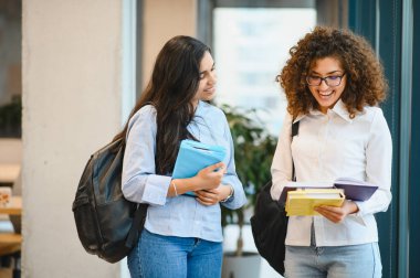Sırt çantaları ve ders kitapları taşıyarak, eğitim ve arkadaşlığı temsil ederek gülümseyen ve sohbet eden çeşitli üniversite öğrencileri