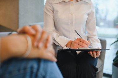 Kadın psikolog bir hastaya danışmanlık yapıyor, bir ruh sağlığı terapisi sırasında not alıyor.