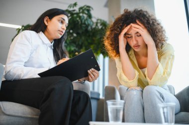 Hintli kadın psikolog terapi seansında stres ve depresyonla boğuşan hastaya profesyonel yardım öneriyor.