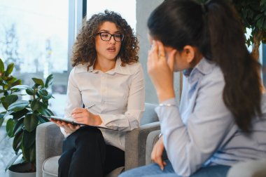 Hintli hastasıyla terapi seansı sırasında stres yaşayan ve zihinsel sağlık desteği arayan bir psikolog not alıyor.