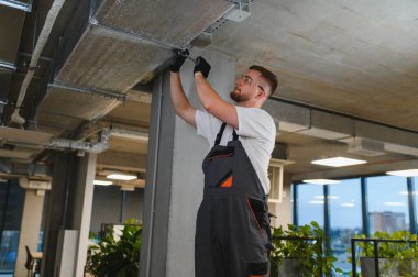 Çağdaş bir ofis ortamında uygun hava kalitesini sağlamak için hvac kanal kurulumu ve bakımı üzerinde çalışan profesyonel teknisyen