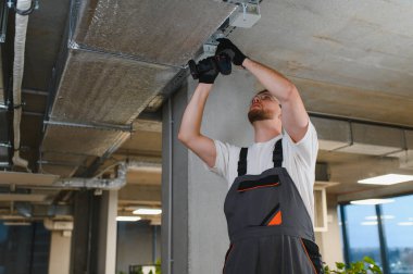 Modern bir ticari binanın ya da endüstriyel tesisin tavanına yeni havalandırma donanımı yerleştiren profesyonel işçiler